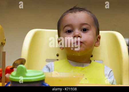 Petit bébé mange avec une cuillère assiette à soupe. Il est assis sur une chaise enfant, mettre foods Banque D'Images