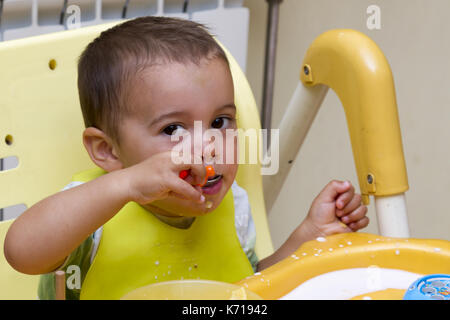 Petit garçon est assis dans une chaise enfant et études ont les repas. La première actions indépendantes de l'enfant. Banque D'Images