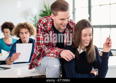Deux étudiants millénaire tout en rire joyeux siégeant ensemble Banque D'Images