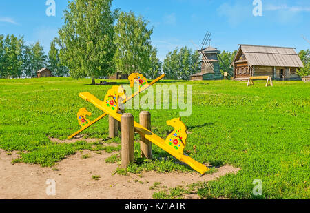 L'aire de jeux sur le pré vert avec balançoires cheval russe traditionnel, décoré de motifs floraux et de Souzdal situé dans l'architecture en bois mu Banque D'Images