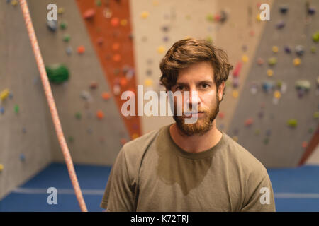 Portrait de l'athlète masculin confiant avec corde en mur d'escalade en salle de sport Banque D'Images