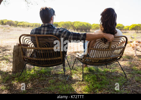 Vue arrière du jeune couple assis sur des chaises sur le terrain Banque D'Images