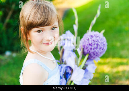 Outdoor portrait of a cute little girl avec beau bouquet de fleurs violettes Banque D'Images