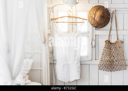 Intérieur de maison en bois moderne à l'intérieur, fenêtre vintage avec volets et rideaux décoratifs. Chapeau de paille, pendaison robe et sac en osier fait main. Banque D'Images