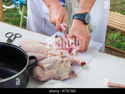 Man's hand holding-couteau et découper le poulet cru sur tableau blanc. la préparation d'ingrédients pour la paella jambalaya, barbecue. à l'extérieur, pique-nique, weeke Banque D'Images