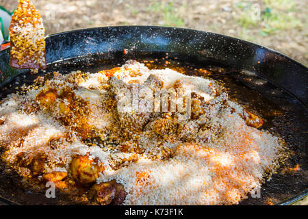 Le Mélange riz non cuit avec sauce tomate et épices lapin frit et la viande de poulet dans une grande poêle plate. la préparation de la paella ou jambalaya. à l'extérieur, s Banque D'Images