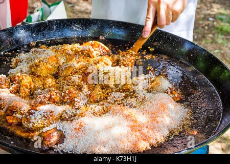 Man's hand holding turner en bois, le mélange riz non cuit avec de la viande de poulet frit à la sauce tomate les épices. la préparation de la paella ou jambalaya. en plein air, pique-nique, f Banque D'Images