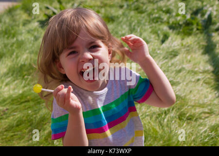 Peu de pretty girl eating lollipop caramel sur fond d'herbe verte et souriante Banque D'Images