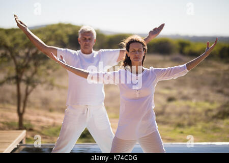 Couple practicing yoga at poolside lors d'une journée ensoleillée Banque D'Images