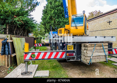 Une grande grue camion stationné dans une ruelle, en location pour soulever des matériaux de construction dans un jardin à proximité. Lincolnshire, Angleterre, Royaume-Uni. Banque D'Images