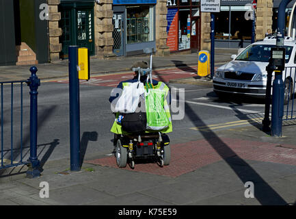 L'homme sur la mobilité scooter crossing road, Huddersfield, Kirklees, West Yorkshire, England UK Banque D'Images