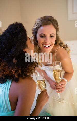 Chuchotant à l'oreille mariée de demoiselle tout en ayant à la maison de champagne dans la chambre Banque D'Images