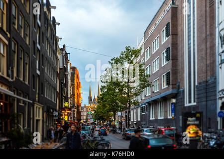 Rue animée d'Amsterdam avec le centre touristique et historique une église avec des spires en arrière-plan alors que le soleil se couche Banque D'Images