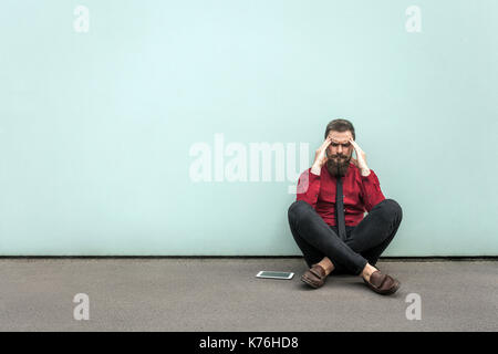 Homme barbu des jeunes adultes se trouve sur le terrain. ont des maux de tête et migraines. Piscine, mur gris. Banque D'Images