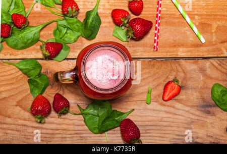 Smoothie aux fraises milkshake ou dans un bocal et les feuilles d'épinards sur fond de bois, des aliments sains pour le petit déjeuner et snack Banque D'Images