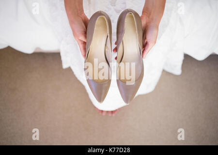 High angle portrait of bride holding shoes tout en restant assis dans la salle de montage Banque D'Images