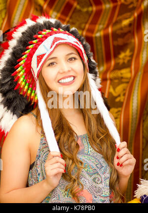 Une belle jeune femme portant Native American hat plume. avec des tissus de couleurs background Banque D'Images