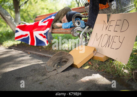 Un homme sans-abri dormant sur banc, mendier de l'argent. Banque D'Images