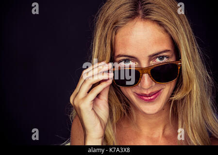 Jeune femme peeking par-dessus des lunettes de soleil, Portrait Banque D'Images