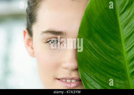 Young woman holding large leaf plus de la moitié de son visage, portrait Banque D'Images