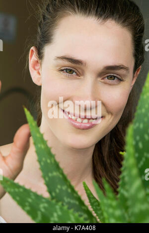 Jeune femme à la recherche grâce à l'usine de vera d'aloès et souriant gaiement Banque D'Images