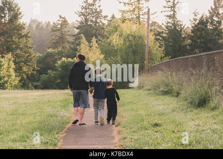 Vue arrière du père et fils marche sur sentier au milieu de terrain herbeux contre des arbres Banque D'Images