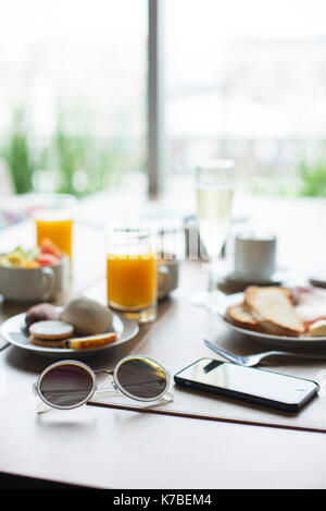 Lunettes de soleil et smartphone sur table de petit-déjeuner dans le café Banque D'Images