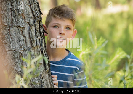 Boy leaning against tree trunk, jusqu'à dans la crainte Banque D'Images