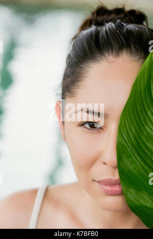 Jeune femme tenant les grandes feuilles en face de son visage et sourire Banque D'Images