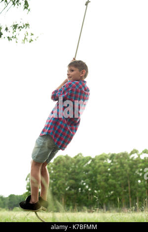 Boy swinging sur corde en plein air Banque D'Images