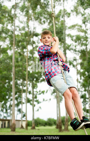 Boy swinging sur corde en plein air Banque D'Images