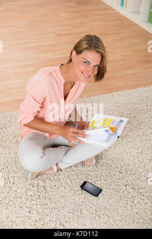 Jeune femme heureuse avec journal assis sur le tapis Banque D'Images