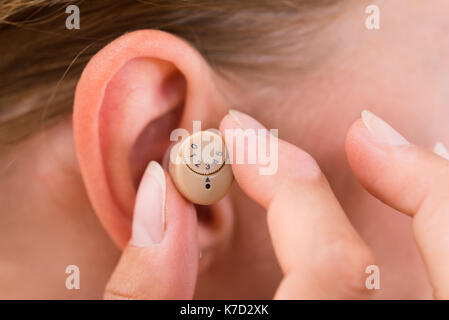 Close-up of female hands mettre dans l'oreille l'aide auditive Banque D'Images