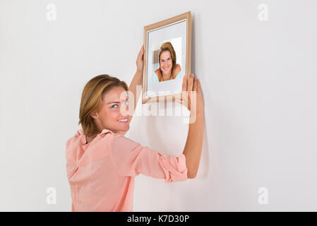 Beautiful happy woman putting image sur mur de chambre Banque D'Images