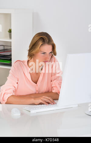 Belle jeune femme heureuse de travailler sur ordinateur de bureau à bureau Banque D'Images