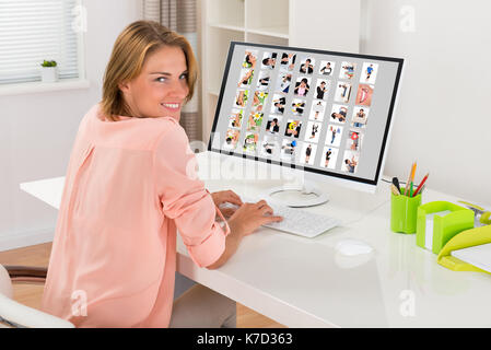 Jeune femme heureuse de travailler avec l'éditeur de photos sur computer in office Banque D'Images