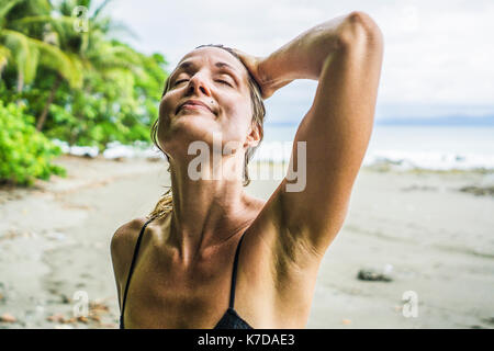 Ambiance Mid adult woman standing with main dans les cheveux humides at beach Banque D'Images