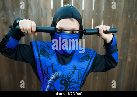 Portrait de jeune garçon en costume de ninja contre permanent clôture en bois Banque D'Images