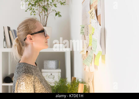 Vue de côté businesswoman reading notes adhésives sur le babillard dans creative office Banque D'Images