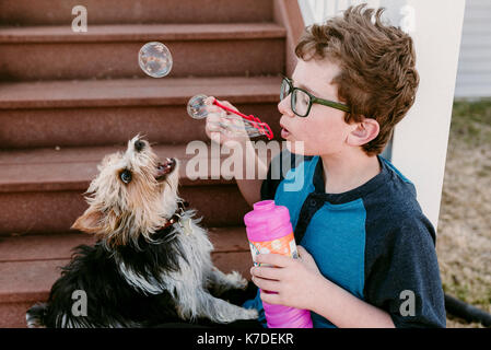 Boy Playing with bubble wand en position assise par chien sur mesures Banque D'Images