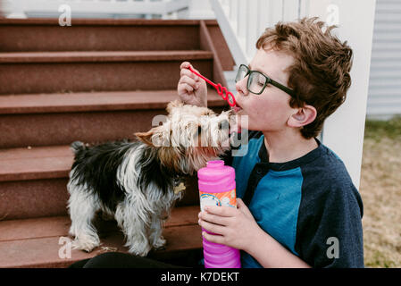 Dog licking boy playing with bubble wand Banque D'Images