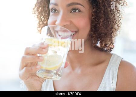 Mid adult woman eau potable avec une tranche de citron. Banque D'Images