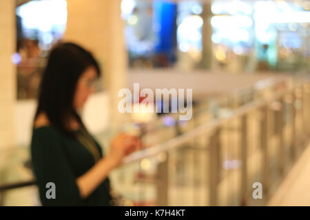 Hors focus shot d'une femme à la recherche de téléphone cellulaire dans la main dans le fashion shopping mall, l'arrière-plan Banque D'Images