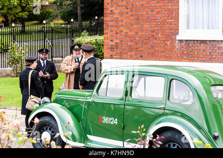 En Angleterre, Chatham Dockyard. Événement, hommage aux années 40. La seconde guerre mondiale, deux officiers de la marine royale et un wren debout dans l'entrée de parler ensemble par deux vert lumineux vintage car. Banque D'Images