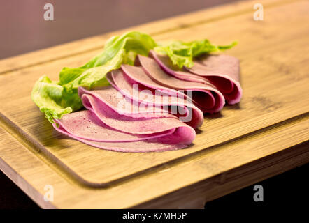 Minces tranches de saucisse avec salade verte sur planche de bois Banque D'Images