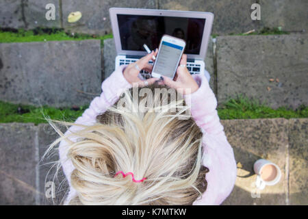 Une fille blonde se repose sur quelques mesures avec son ordinateur portable, téléphone mobile, une cigarette et une tasse de thé Banque D'Images