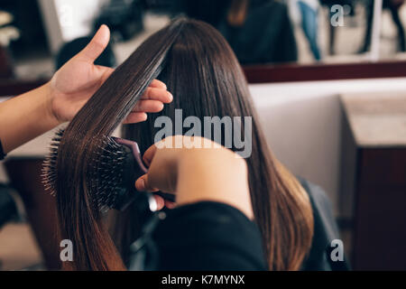 Coiffeur professionnel styling les cheveux d'un client au salon de coiffure. Styliste de cheveux des femmes peigner les cheveux à l'aide d'une brosse à cheveux. Banque D'Images