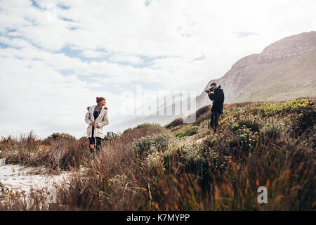 Jeune couple en vacances prendre des photos. L'homme à prendre des photos de jeune femme debout à l'extérieur dans la nature. Banque D'Images