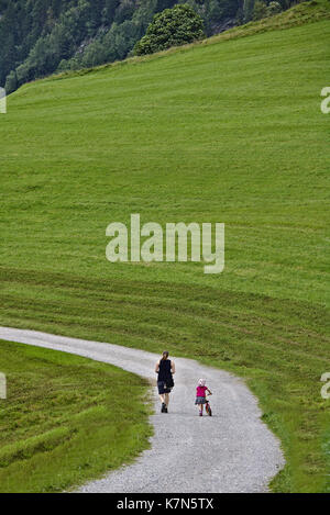 Femme et petite fille avec Strider Vélo et casque de derrière la marche le long d'une piste de gravier dans un champ vert Banque D'Images