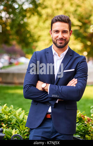 Un beau jeune businessman standing et d'attente sur le côté d'un parc Banque D'Images